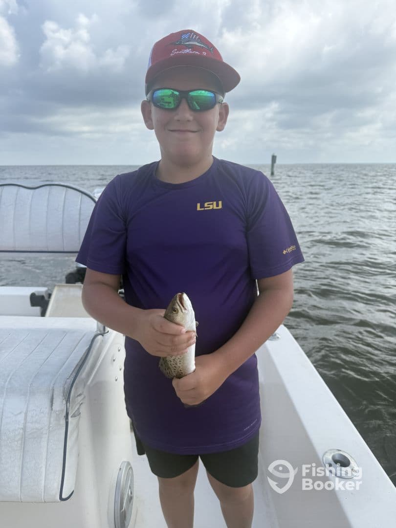 A young angler proudly displaying a speckled trout while fishing on a boat, showcasing a fun day on the water.