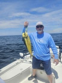 An angler proudly displaying a vibrant Mahi Mahi while fishing offshore, showcasing a sunny day on the water.