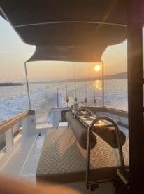 Interior view of a boat showcasing comfortable seating and fishing rods against a sunset backdrop, ideal for a relaxing fishing trip.