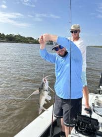 Angler reeling in a Catfish while fishing on a sunny day in a coastal waterway.