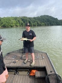 A young angler proudly displaying a caught fish while fishing from a boat in a scenic river setting.