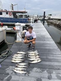 A young angler proudly displaying a successful catch of multiple fish on the dock, showcasing a variety of species after a day of fishing.