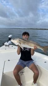 Young angler proudly holding a large Redfish while on a boat, showcasing a successful fishing trip.