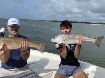 A father and son proudly displaying their catch of Redfish while enjoying a day on the water.