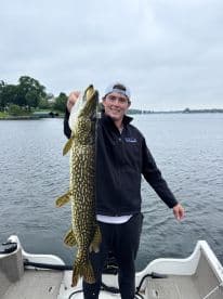 A young angler proudly displaying a Northern Pike while fishing from a boat on a calm lake.