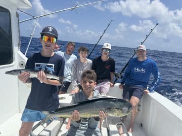 A group of young anglers proudly displaying their catch, including a large Mahi Mahi and a Barracuda, while enjoying a day of deep-sea fishing.