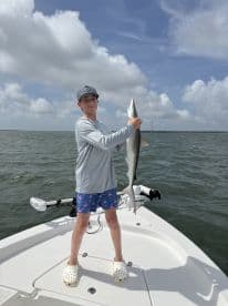 Young angler proudly holding a shark on the bow of a boat during a fishing trip.