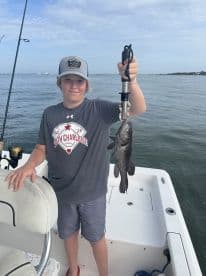 Young angler proudly holding a Black Sea Bass while fishing on a boat, showcasing a successful catch during a day on the water.