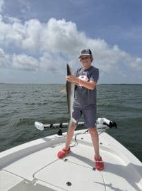 Young angler proudly holding a shark while fishing on a boat in a coastal environment.