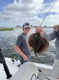 A young angler proudly displaying a caught stingray while fishing from a boat in a coastal waterway.