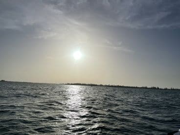 A scenic view of the water with the sun setting in the background, showcasing a tranquil fishing environment.