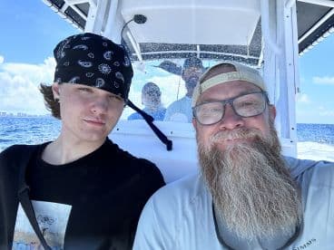 A young angler and an adult enjoying a sunny day on a fishing boat, showcasing the interior seating area while heading out to sea.