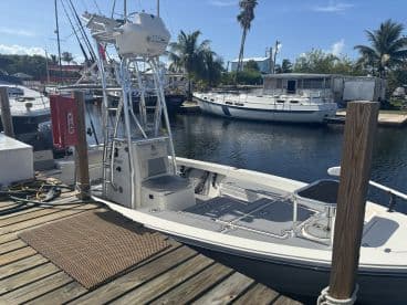A sleek fishing boat docked at a marina, showcasing its tower and spacious deck, surrounded by palm trees and other vessels.