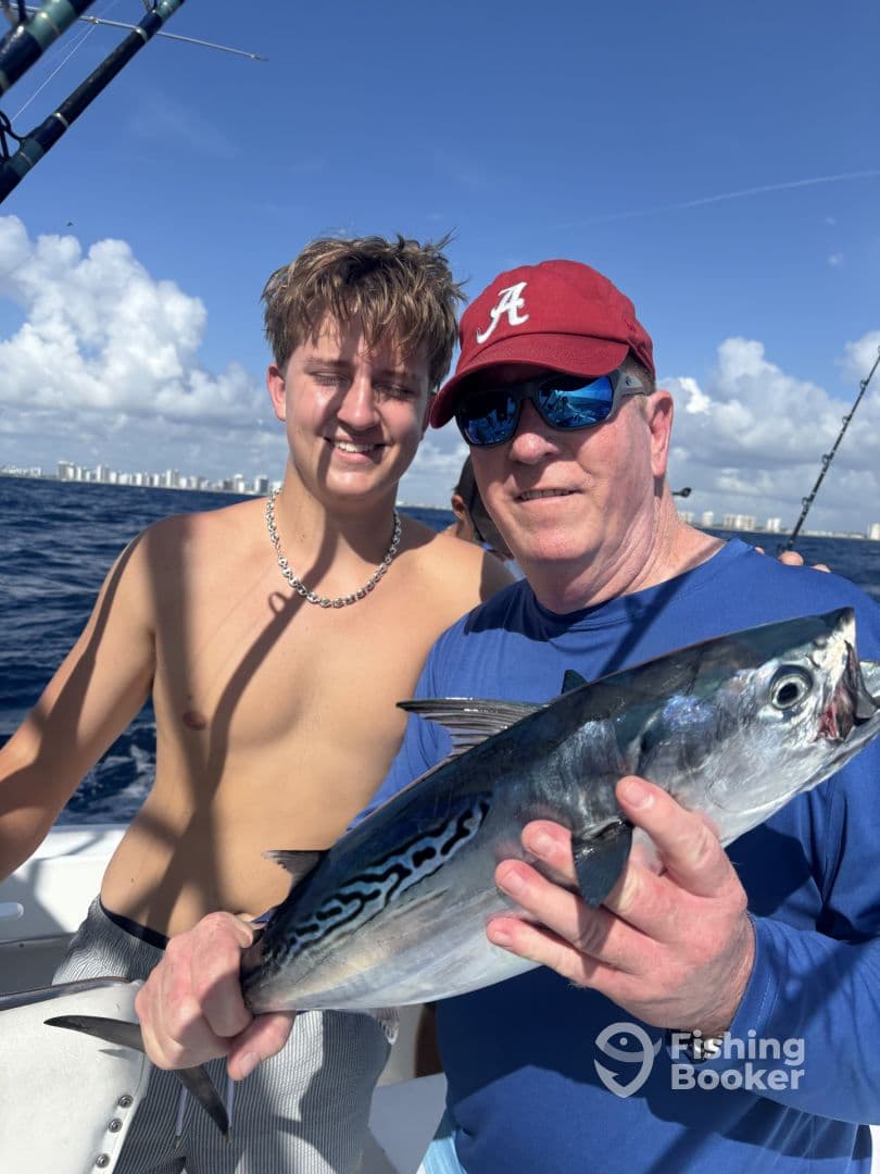 A young angler and an adult proudly displaying a large Bonito while fishing offshore, enjoying a sunny day on the water.