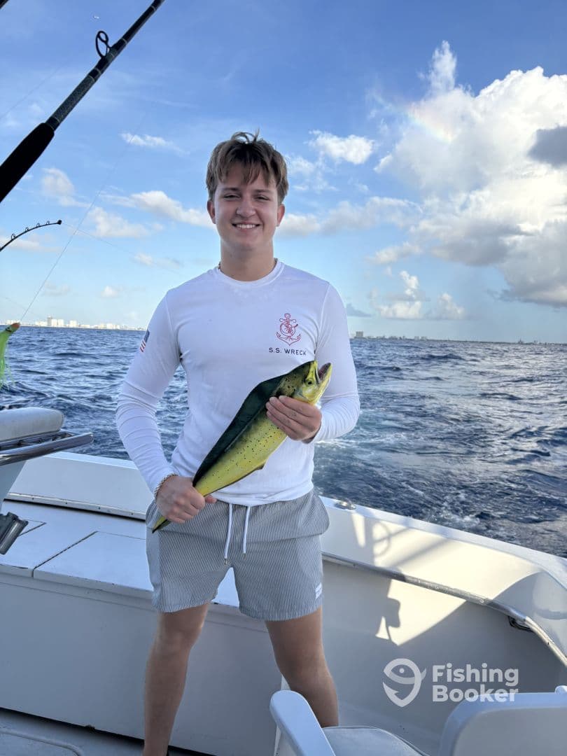A young angler proudly displaying a vibrant Mahi Mahi aboard a fishing boat in clear blue waters.