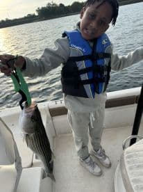A young angler proudly displaying a striped bass while fishing on a boat, showcasing a fun day on the water.