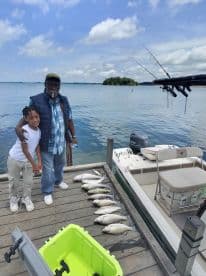 A young boy and his grandfather proudly pose together at the dock, showcasing their catch of striped bass after a successful fishing trip.