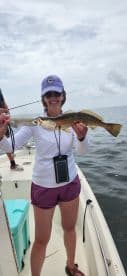 An angler proudly displaying a large Speckled Trout while fishing on a boat in open waters.