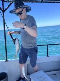 Angler reeling in two fish while fishing on a boat in clear blue waters, showcasing a successful catch.