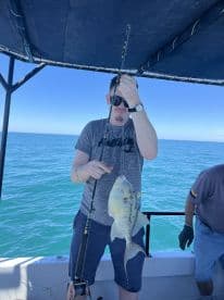Angler reeling in a large fish while fishing on a boat in clear blue waters, showcasing a successful catch.