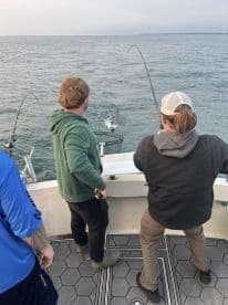 Two anglers actively reeling in fish from the boat, showcasing the excitement of a fishing trip on open waters.