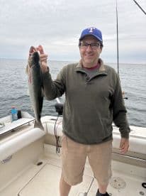 An angler proudly displaying a freshly caught Speckled Trout while fishing on a boat in open waters.