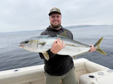 Angler proudly displaying a large Yellowtail while fishing from a boat in open waters.