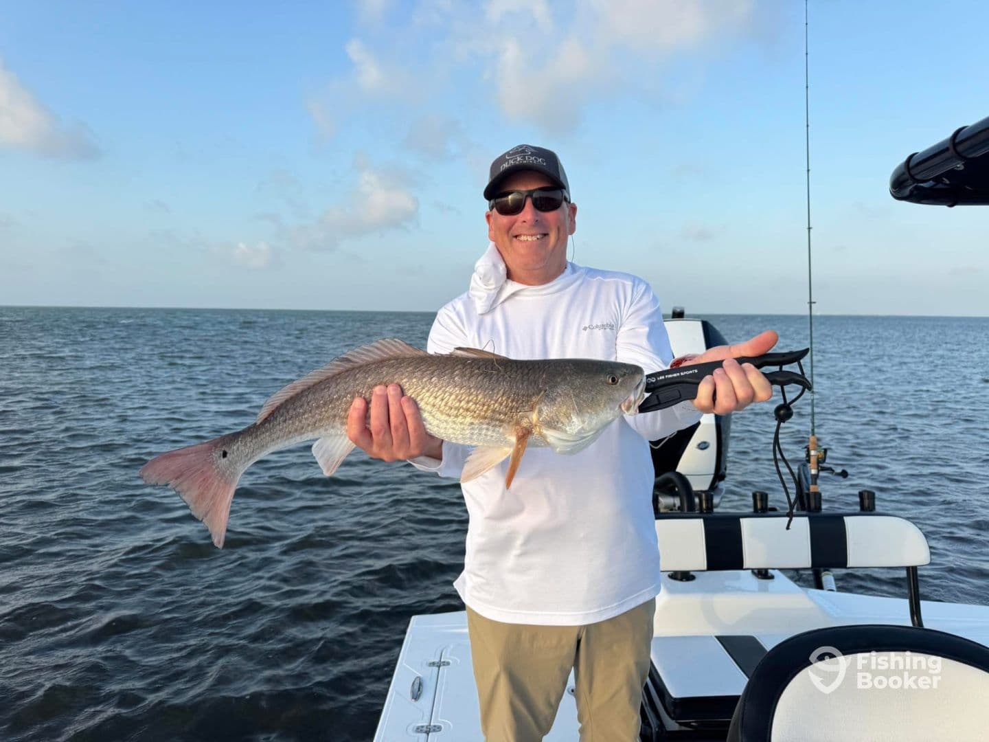 An angler proudly displaying a large Redfish while fishing on a boat in open waters.