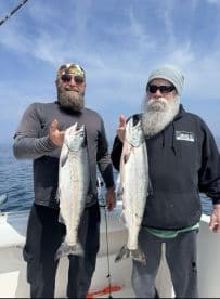 Two anglers proudly displaying their catch of Salmon while fishing on a boat, showcasing a successful day on the water.
