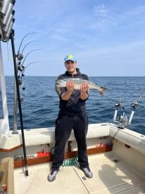 Young angler proudly displaying a caught fish on a fishing boat, surrounded by fishing rods, in a scenic ocean setting.