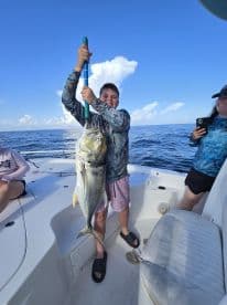 A young angler proudly displaying a large Jack Crevalle while fishing on a boat in open waters.