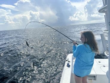 A young angler is actively reeling in a fish while fishing on a boat, showcasing the excitement of the catch in open waters.