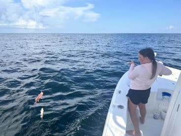 A young angler is reeling in two fish while fishing off the coast, showcasing an exciting moment on the water.