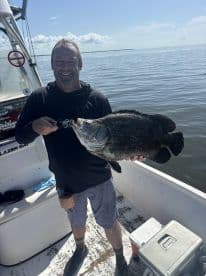 Angler proudly displaying a large Black Drum while fishing on a Blazer Bay boat in calm waters.