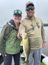 Two anglers proudly displaying a Walleye caught during a fishing trip on a calm lake.