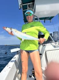 An angler proudly displaying a large King Mackerel while fishing offshore, showcasing the vibrant colors of the fish against a clear blue sky.