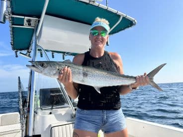 An angler proudly displaying a large King Mackerel while fishing on a boat in clear waters.