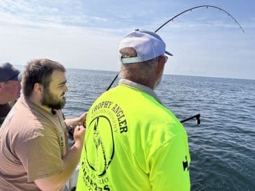 Three anglers engaged in a fishing battle on a sunny day, with one actively reeling in a catch off the coast of Lake Ontario.