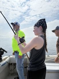 A young angler is actively reeling in a fish while fishing on a boat, with two adults nearby, showcasing a lively fishing experience.