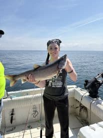 A young angler proudly displaying a large Lake Trout while fishing on a boat in open water.