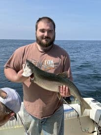 Angler proudly displaying a large Lake Trout while fishing on a boat, showcasing a sunny day on the water.