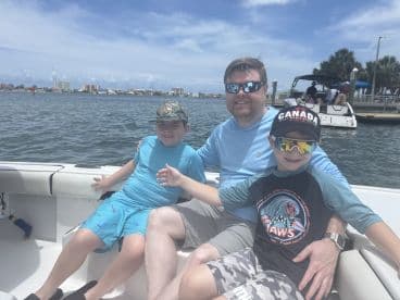 A father and two young boys enjoying a sunny day on a boat, showcasing a family-friendly fishing experience in a coastal setting.