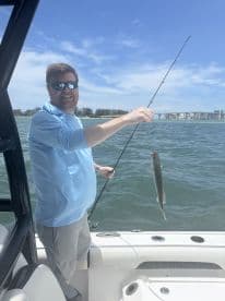 Angler reeling in a Speckled Trout while enjoying a sunny day on the water, showcasing the excitement of fishing.