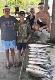 A group of young anglers proudly posing with their catch of Redfish displayed on a cleaning table after a successful fishing trip.