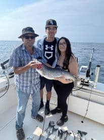 A family proudly displaying a large Lake Trout on a fishing charter, with several smaller fish visible on the deck.