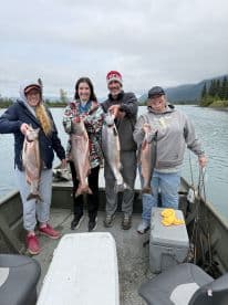 A group of four anglers proudly displaying their catch of salmon while fishing from a boat in a scenic river setting.