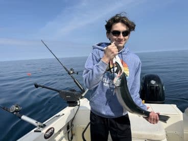 A young angler proudly displaying a caught fish while fishing on a calm day at sea, showcasing a serene fishing environment.