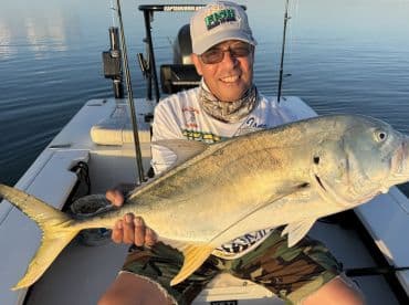 Angler proudly displaying a large Jack Crevalle on a fishing boat, showcasing a successful day on the water.