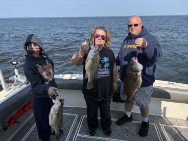 A family enjoying a successful fishing trip, proudly displaying their catch of two large fish while aboard a fishing boat.