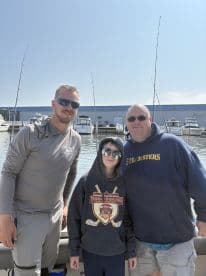 A group of three individuals, including a child, posing on a fishing boat with a marina backdrop, showcasing a relaxed fishing atmosphere.